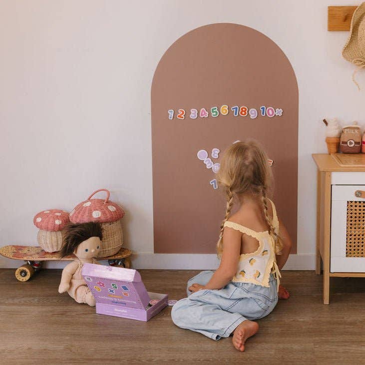 Child playing with a toy on the floor next to a wall with colorful numbers.