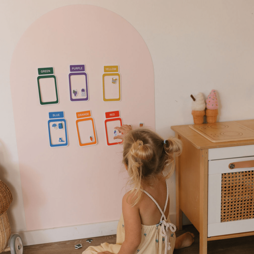 Child interacting with colorful labels on a pink wall in a child-friendly room.