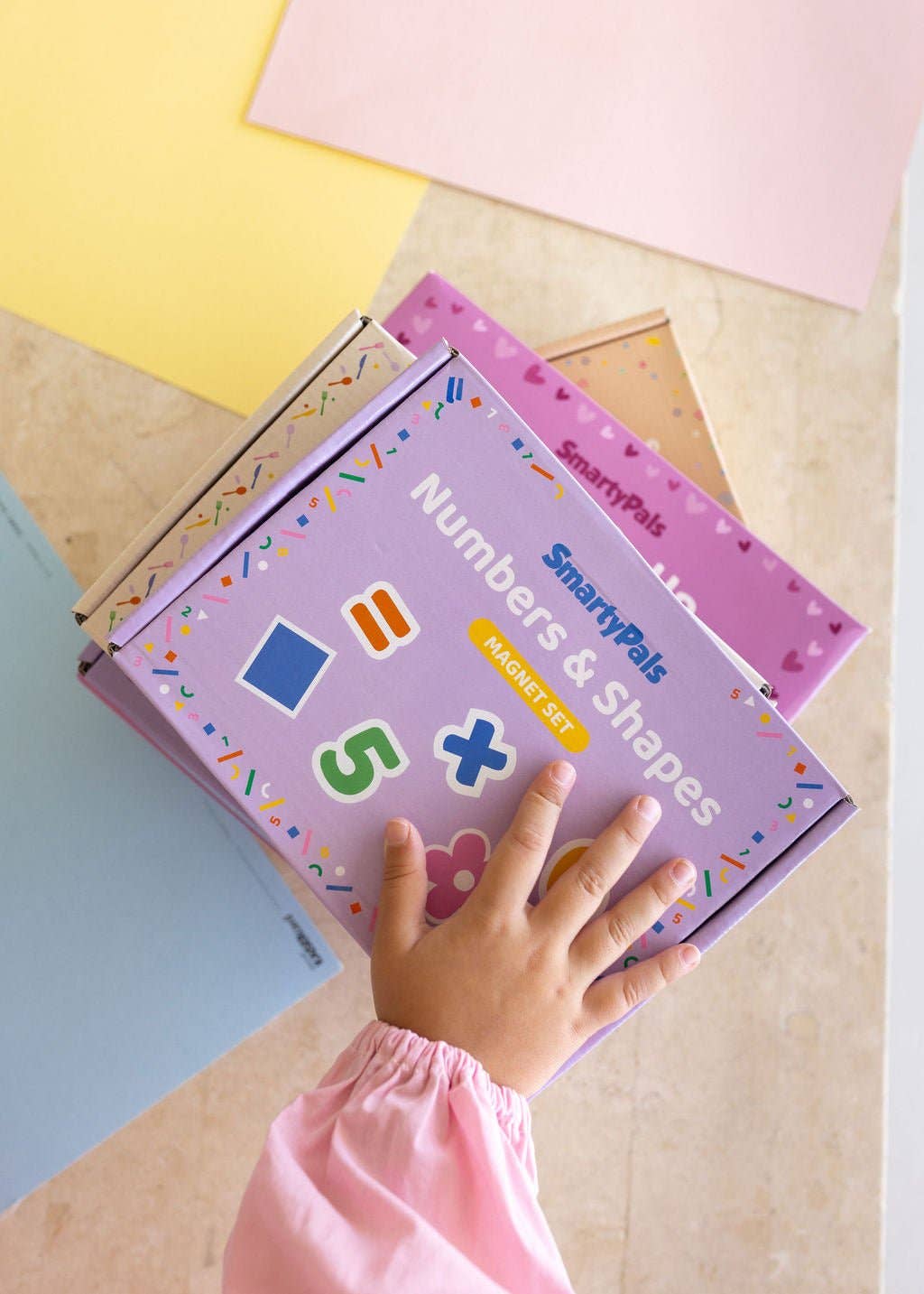 Child's hand on a SpartyPals Numbers & Shapes book on a colorful surface
