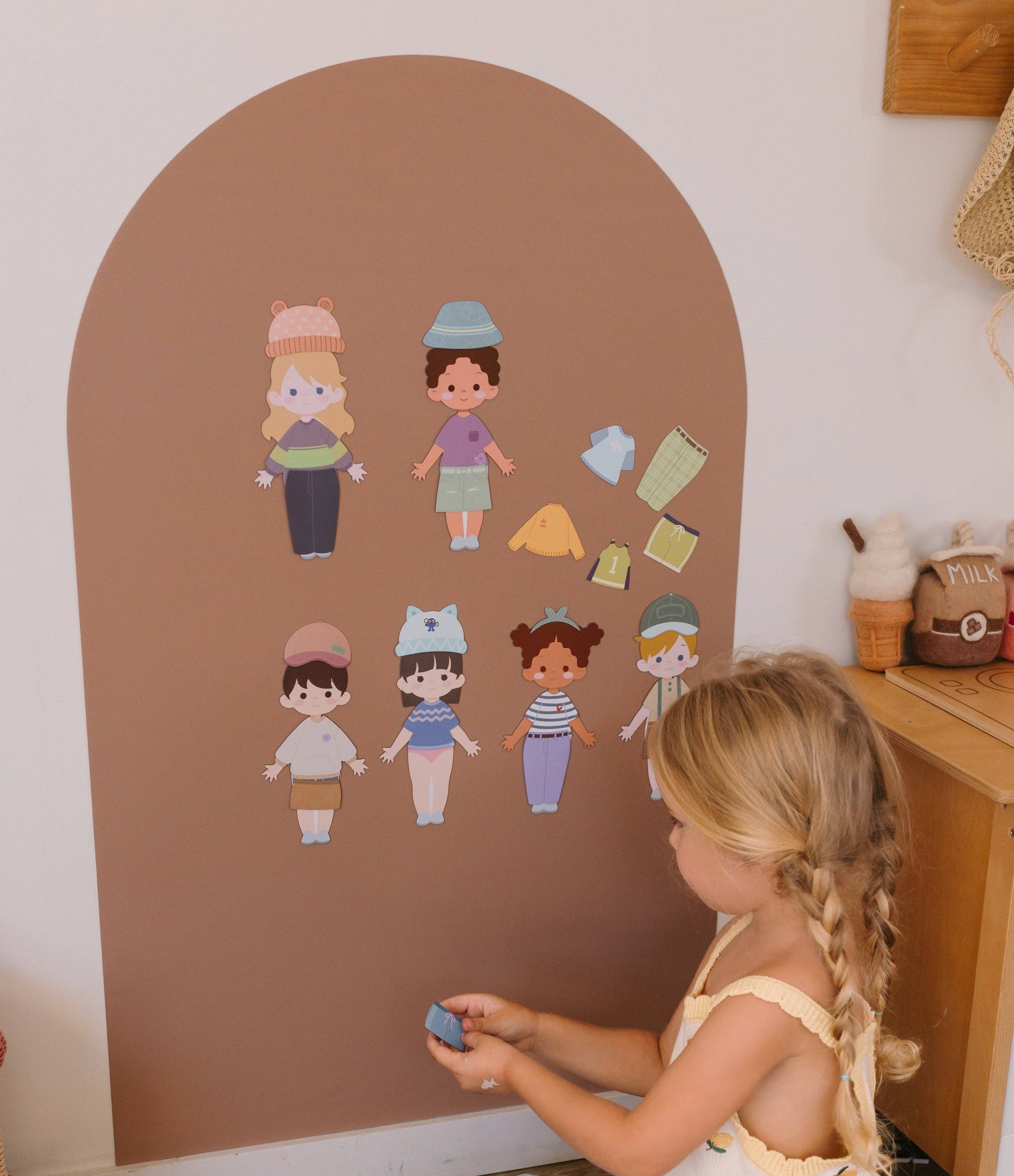 Child playing with dress-up figures on a wall with an arch-shaped brown background