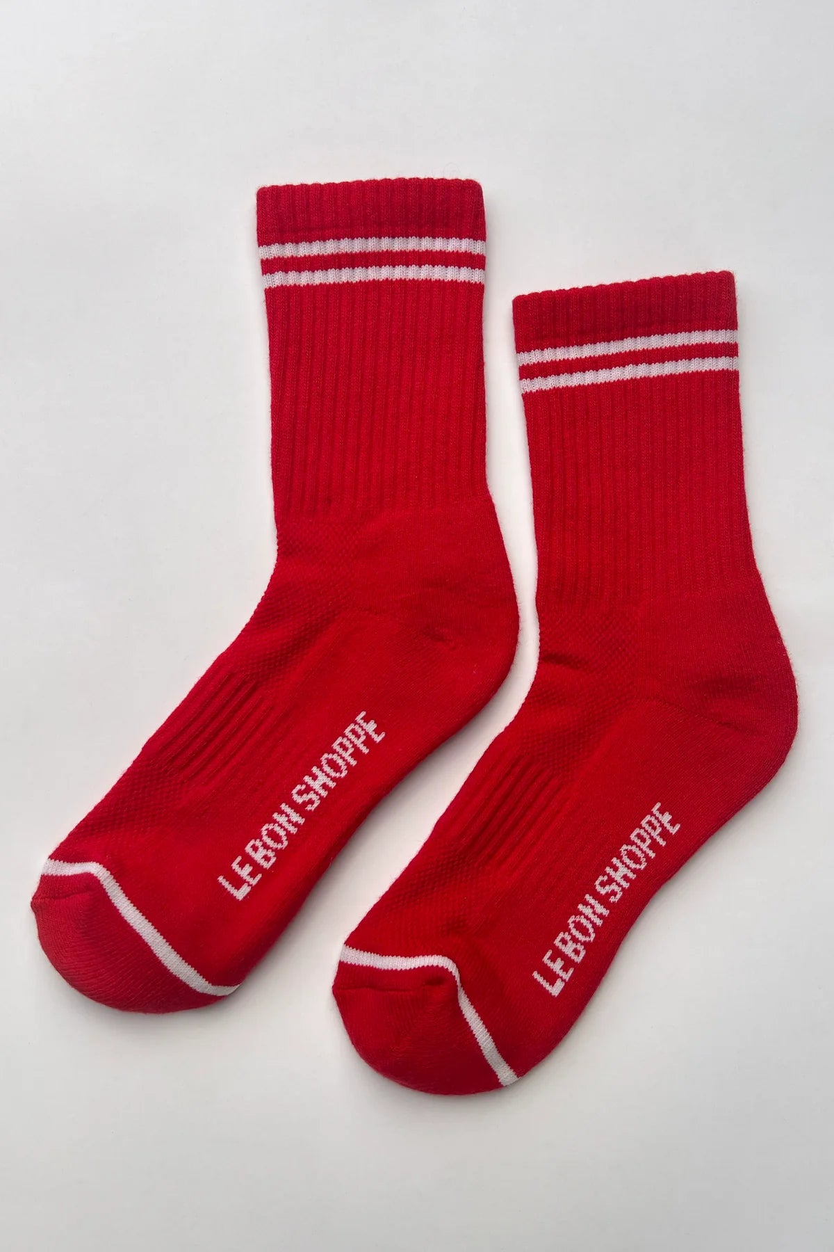 Red socks with white stripes and 'Le Bon Shoppe' branding on a light gray background