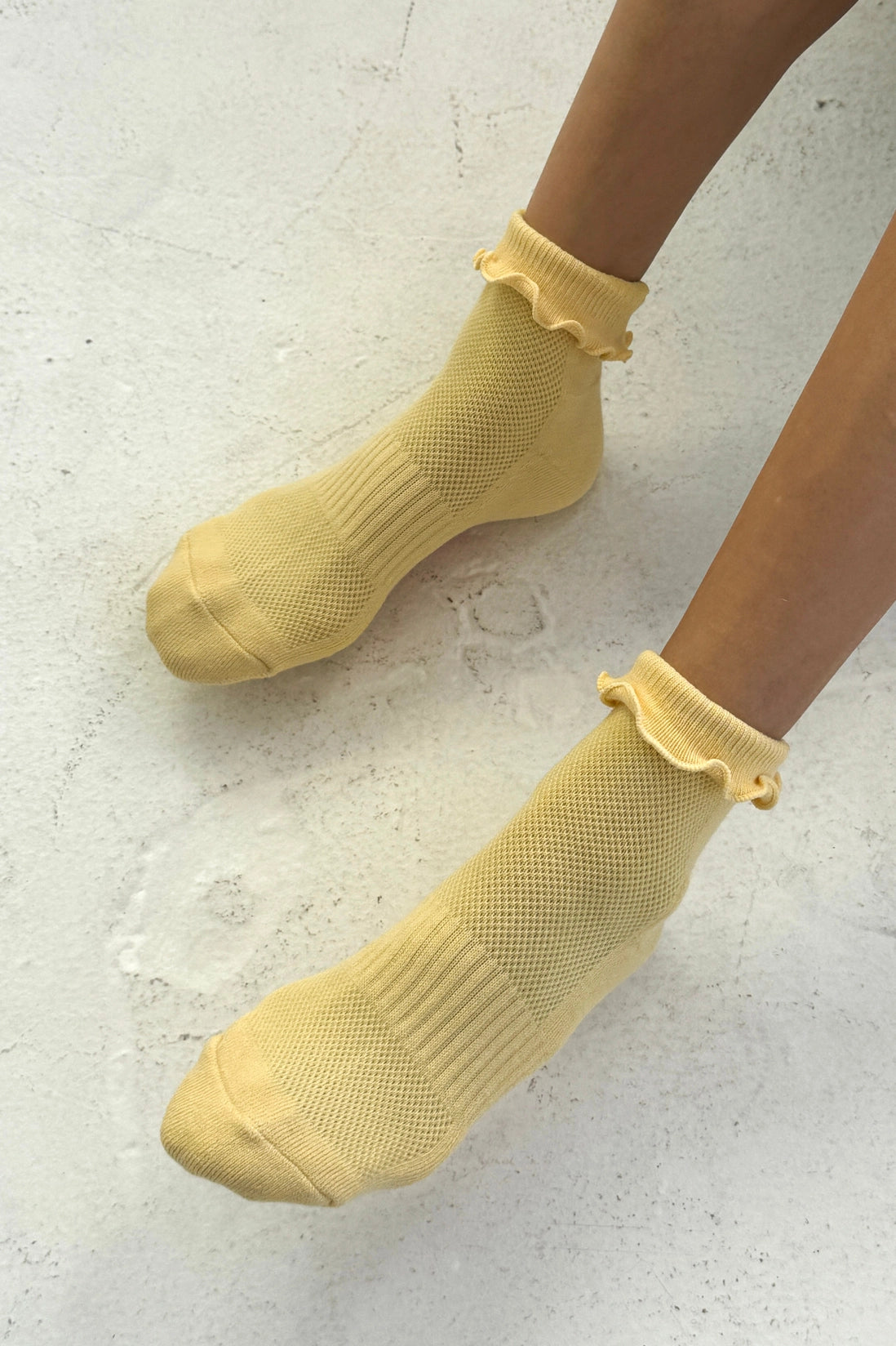 Yellow socks with ruffled top worn by a person on a light gray background