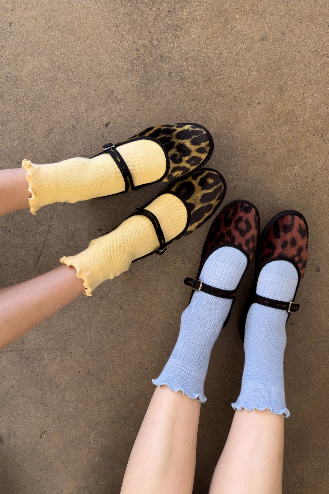 Two pairs of feet wearing leopard print shoes and colorful socks on a concrete floor.