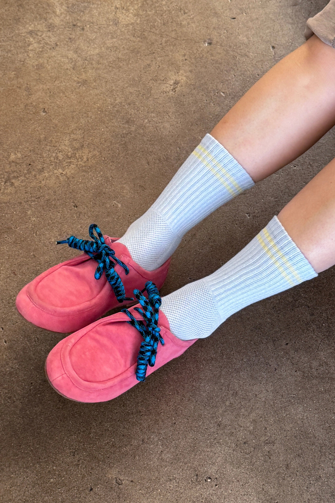 Pink slippers with blue laces worn with light blue socks on a concrete floor.