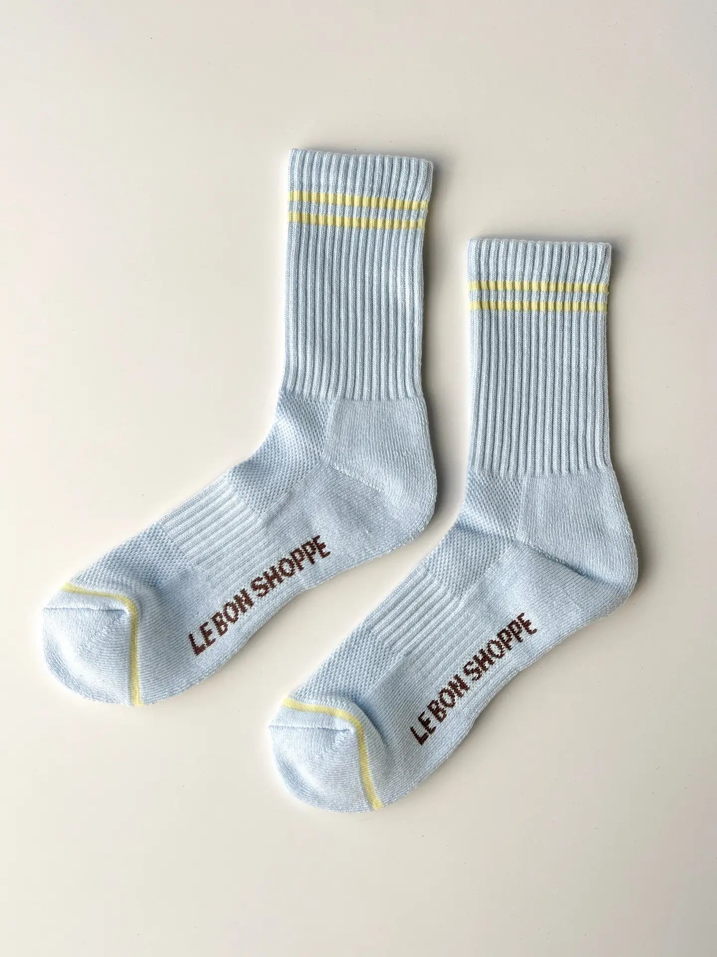 Pair of light blue socks with yellow accents and 'Lebon Shoppe' branding on a beige background