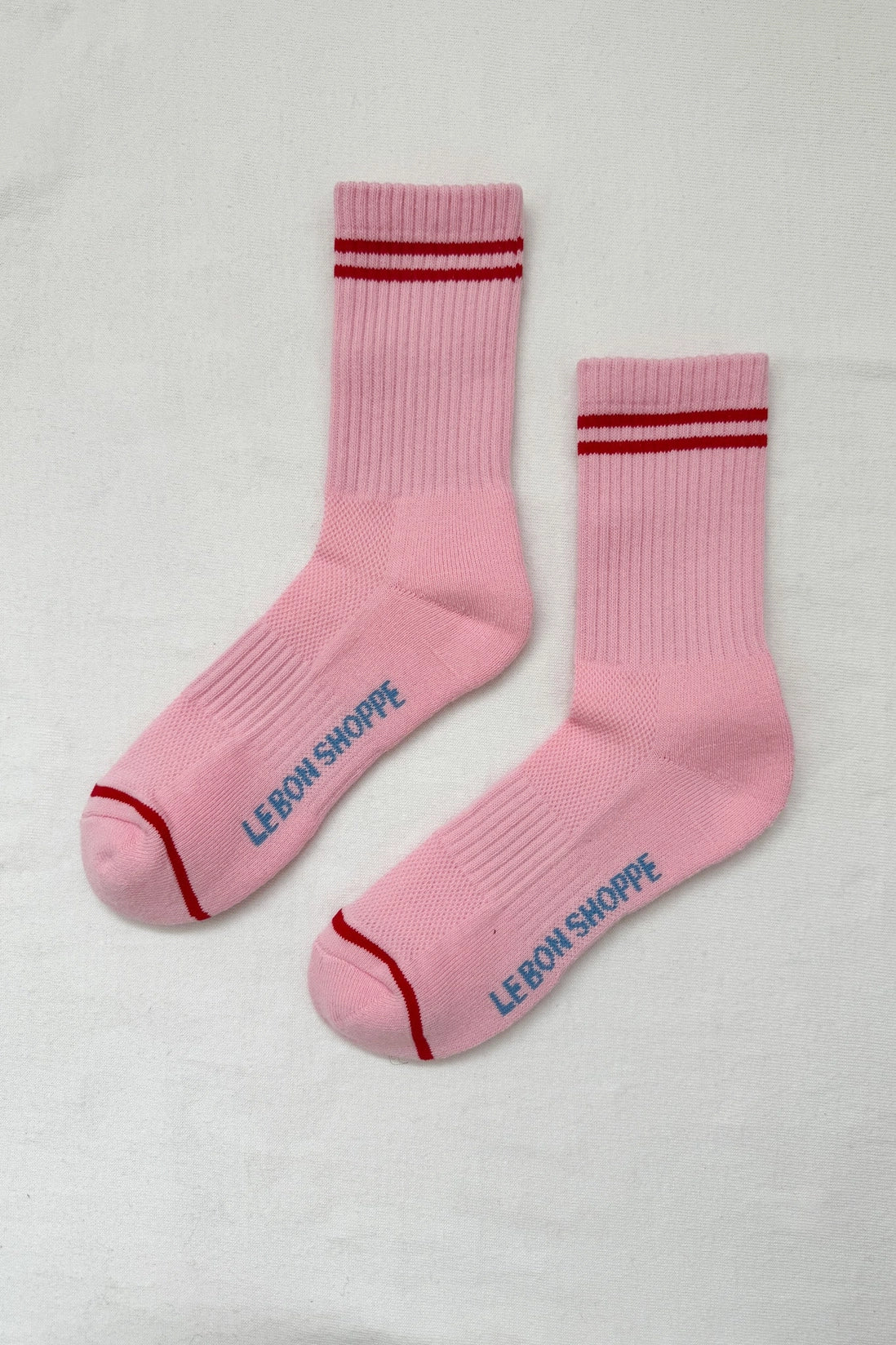 Pair of pink socks with red stripes and 'Le Bon Shoppe' branding on a white background
