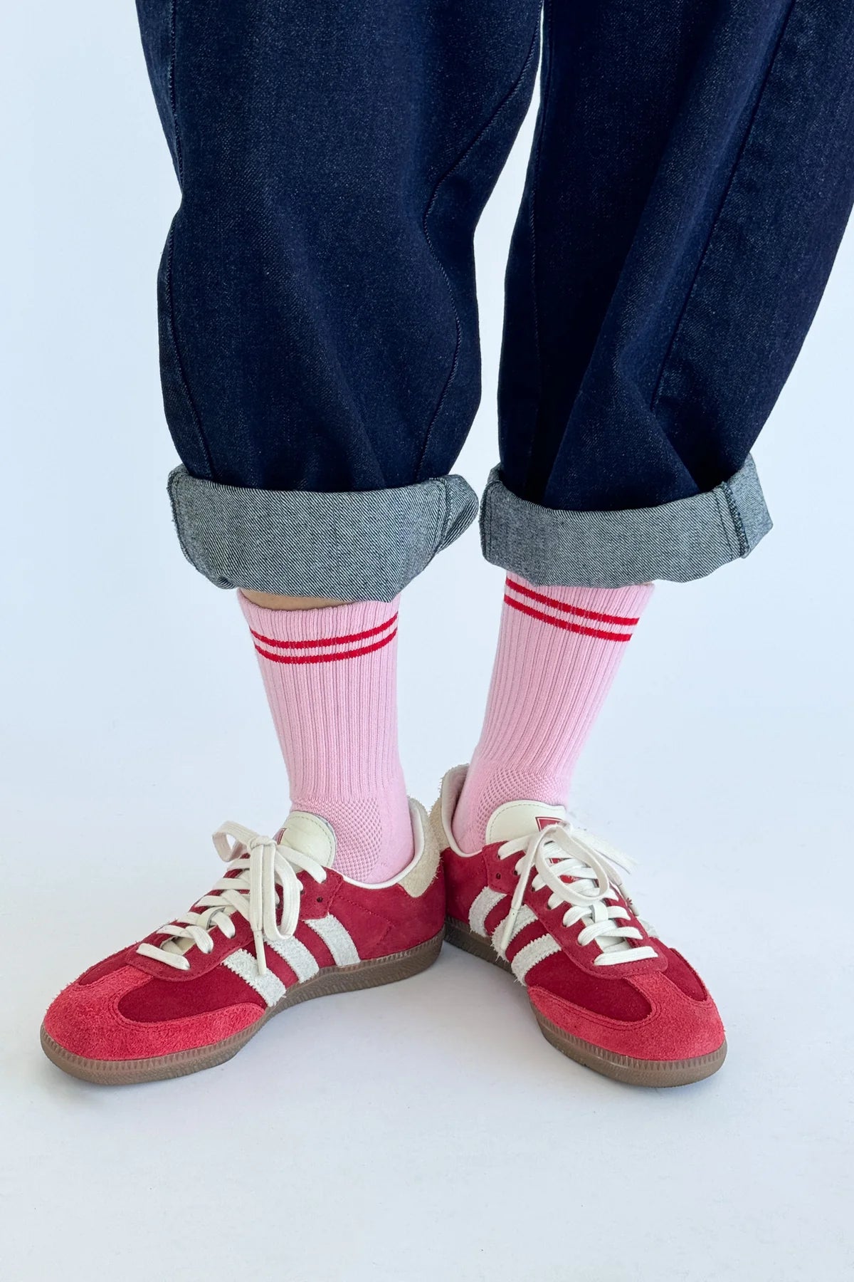 Person wearing red sneakers with white laces, pink socks with red stripes, and rolled-up jeans on a light background.