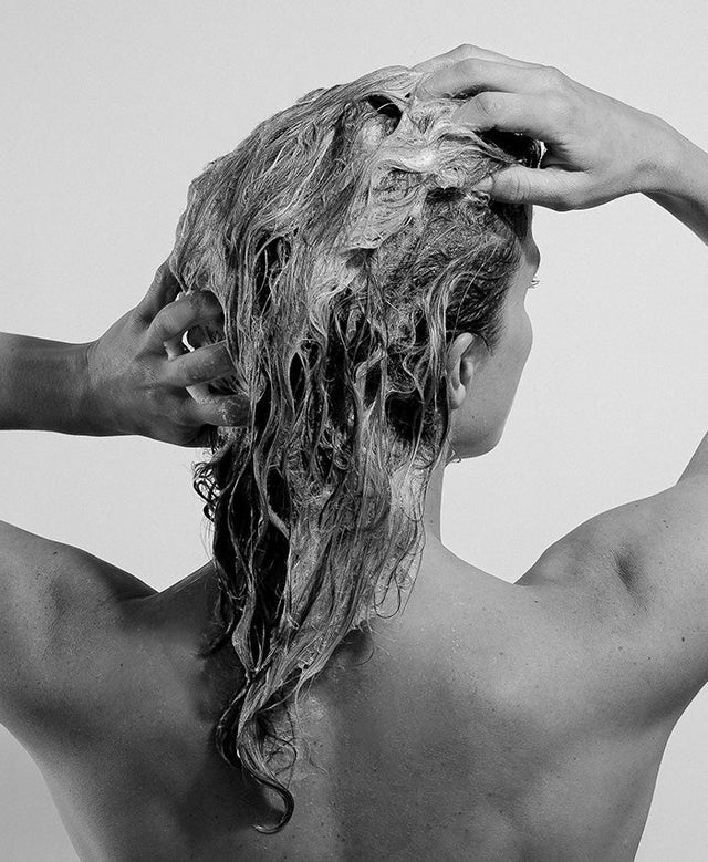 Person washing their hair with hands on a plain background