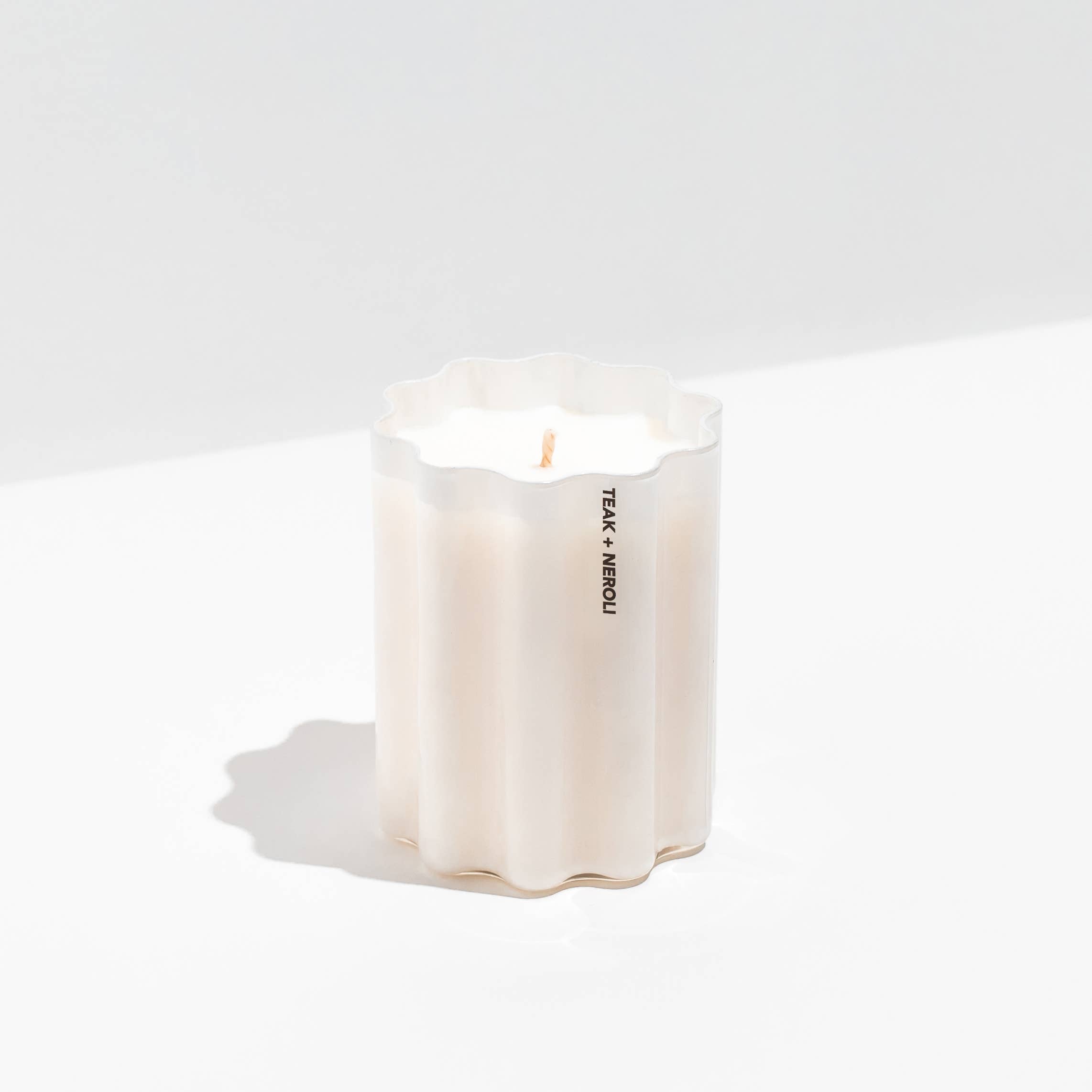 A white scented candle in a fluted, scalloped glass container with a single wick. The container features vertical black text reading 'TALK + NEROLI' on the front.