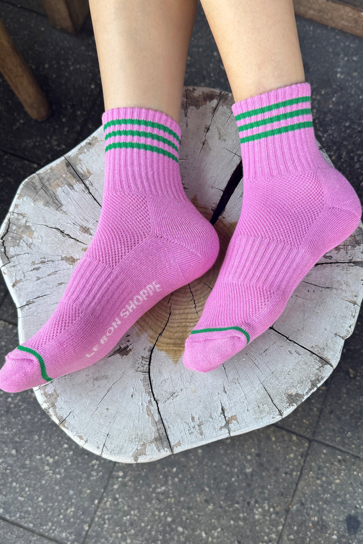 Pink socks with green stripes worn by a person on a tree stump.