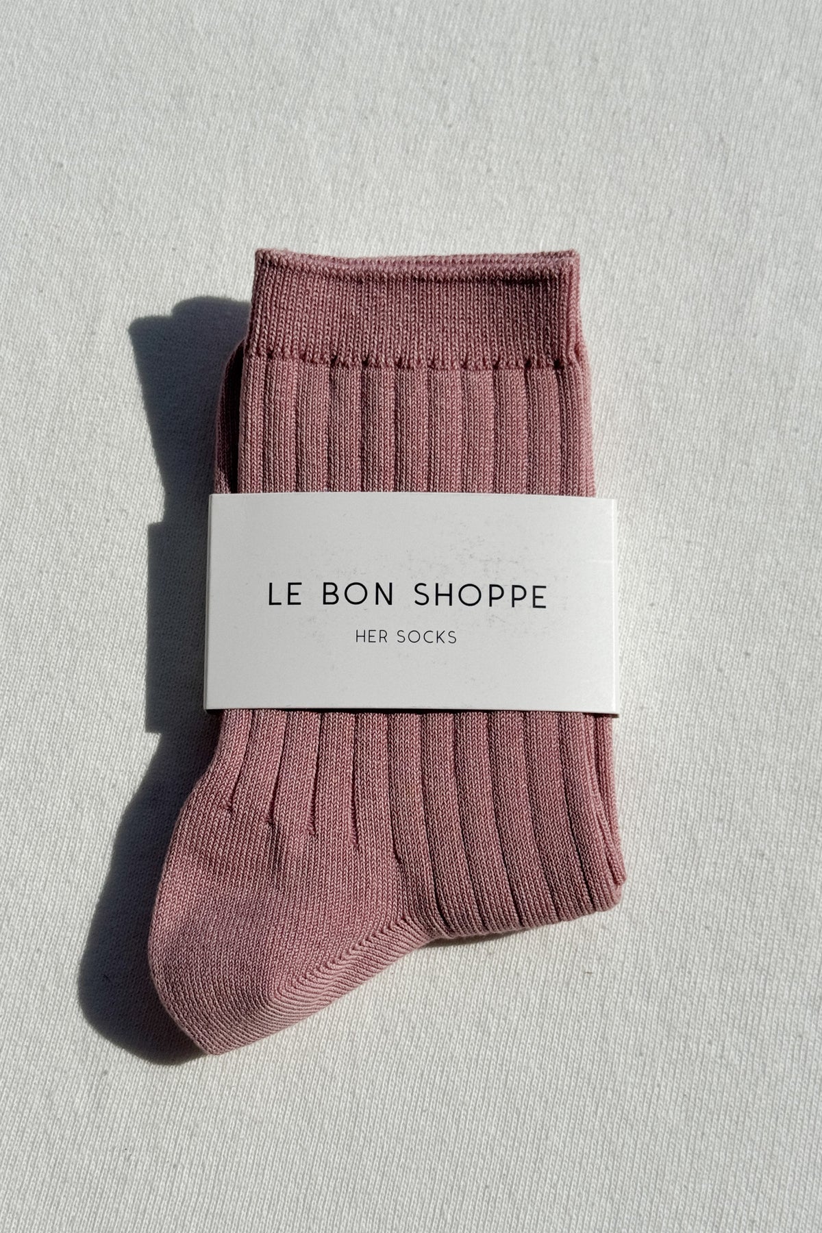 Packaged pink socks with 'Le Bon Shoppe' label on a light gray background