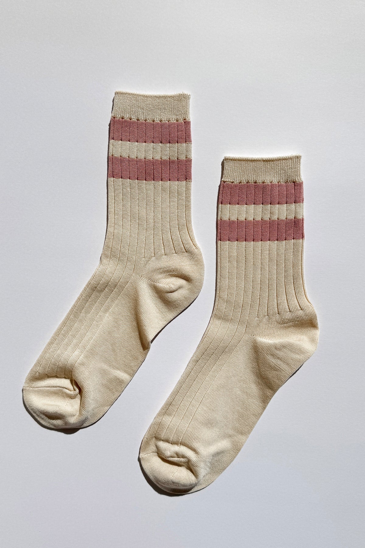 Pair of beige socks with pink stripes on a light gray background