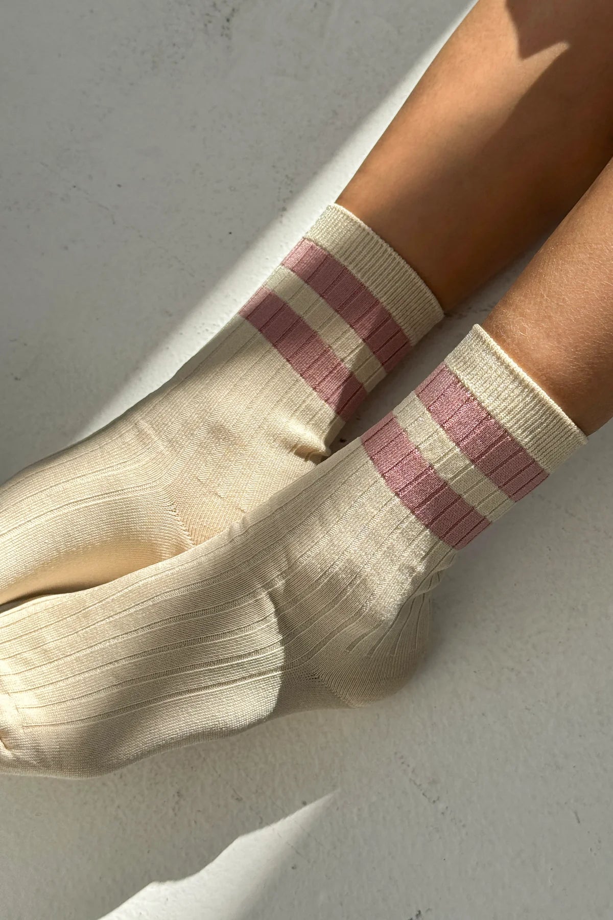 Beige socks with pink stripes worn by a person on a light gray background