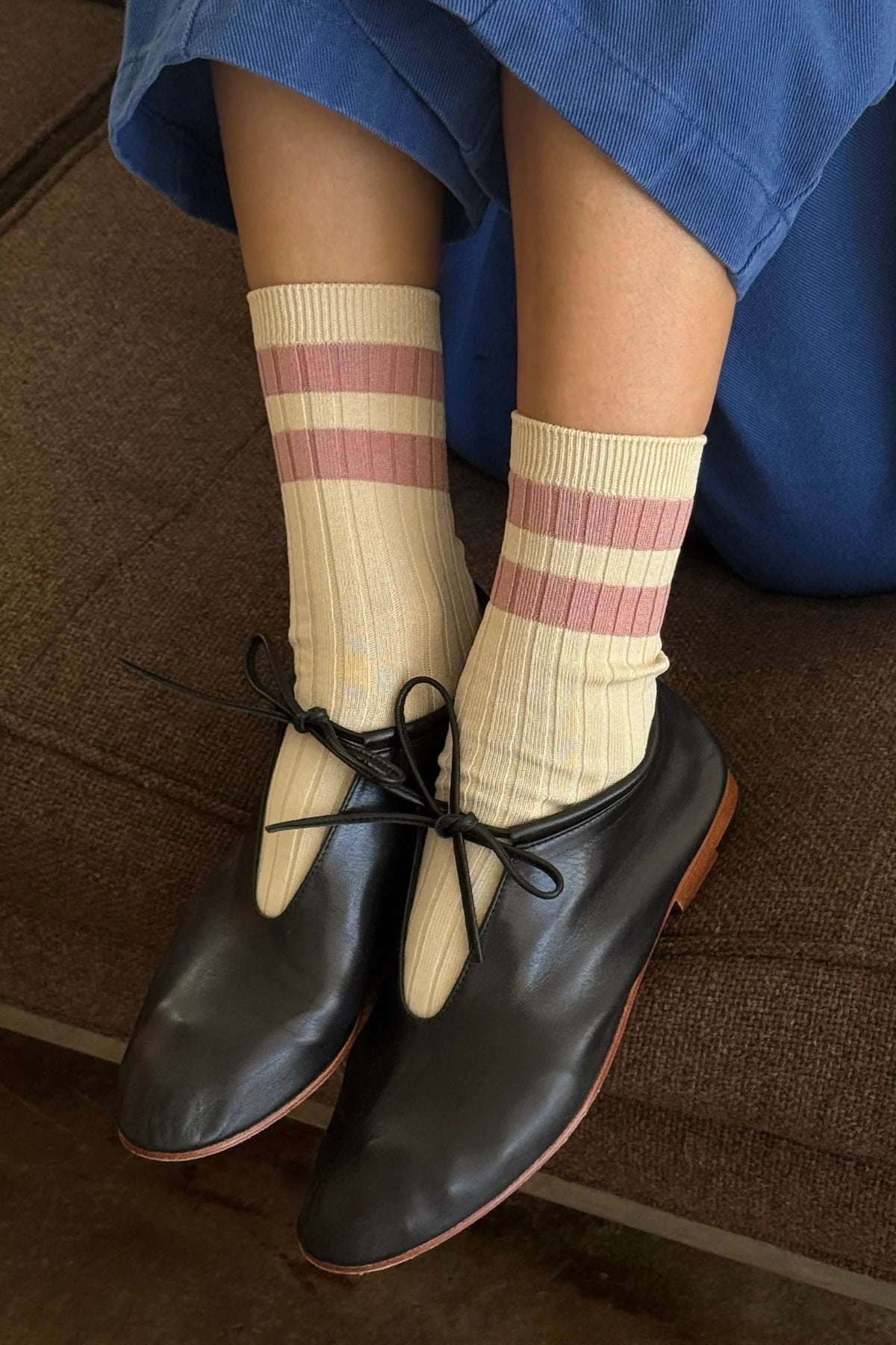 Person wearing black shoes and beige socks with pink stripes on a wooden floor.