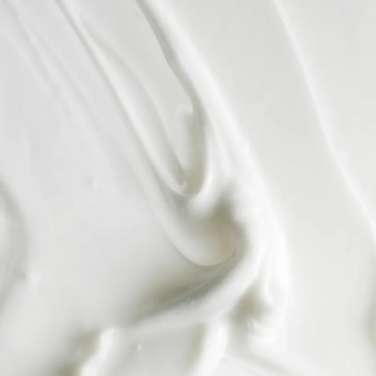 A close-up texture shot of a thick, creamy white cosmetic cream with smooth, swirled folds.