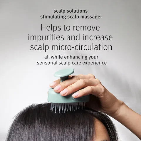 A hand using a mint green scalp massager on dark hair, with promotional text above reading 'scalp solutions stimulating scalp massager' and 'Helps to remove impurities and increase scalp micro-circulation'.