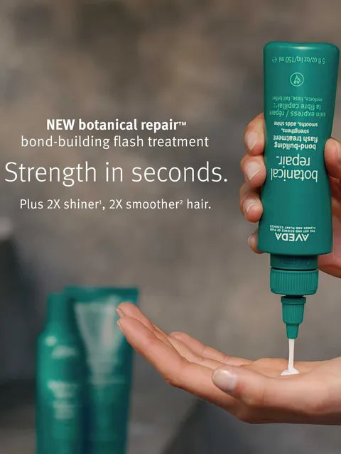 A hand holds a teal squeeze bottle of Aveda Botanical Repair bond-building flash treatment over an open palm, with white cream being dispensed. Large promotional text appears on the left, and two blurred bottles appear in the background.