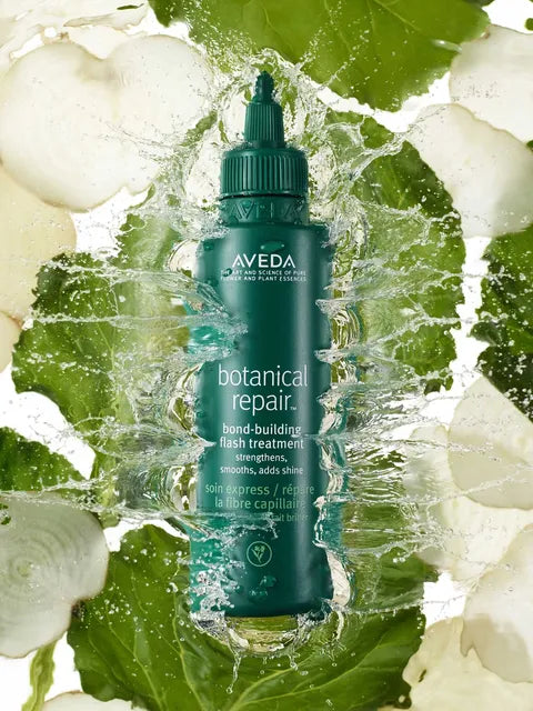 Aveça Botanical Repair Bond-Building Flash Treatment in a dark teal squeeze bottle, surrounded by a dynamic water splash and fresh green leaves.