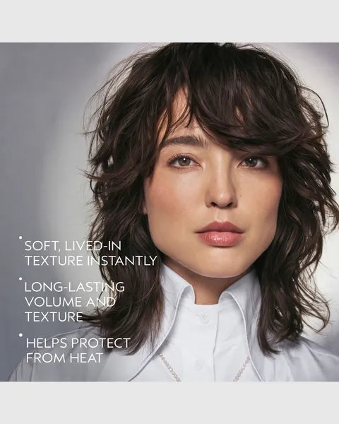 A close-up portrait of a woman with dark brown, layered, textured hair wearing a white collared shirt. White text on the left reads: 'SOFT, LIVED-IN TEXTURE INSTANTLY', 'LONG-LASTING VOLUME AND TEXTURE', and 'HELPS PROTECT FROM HEAT'.