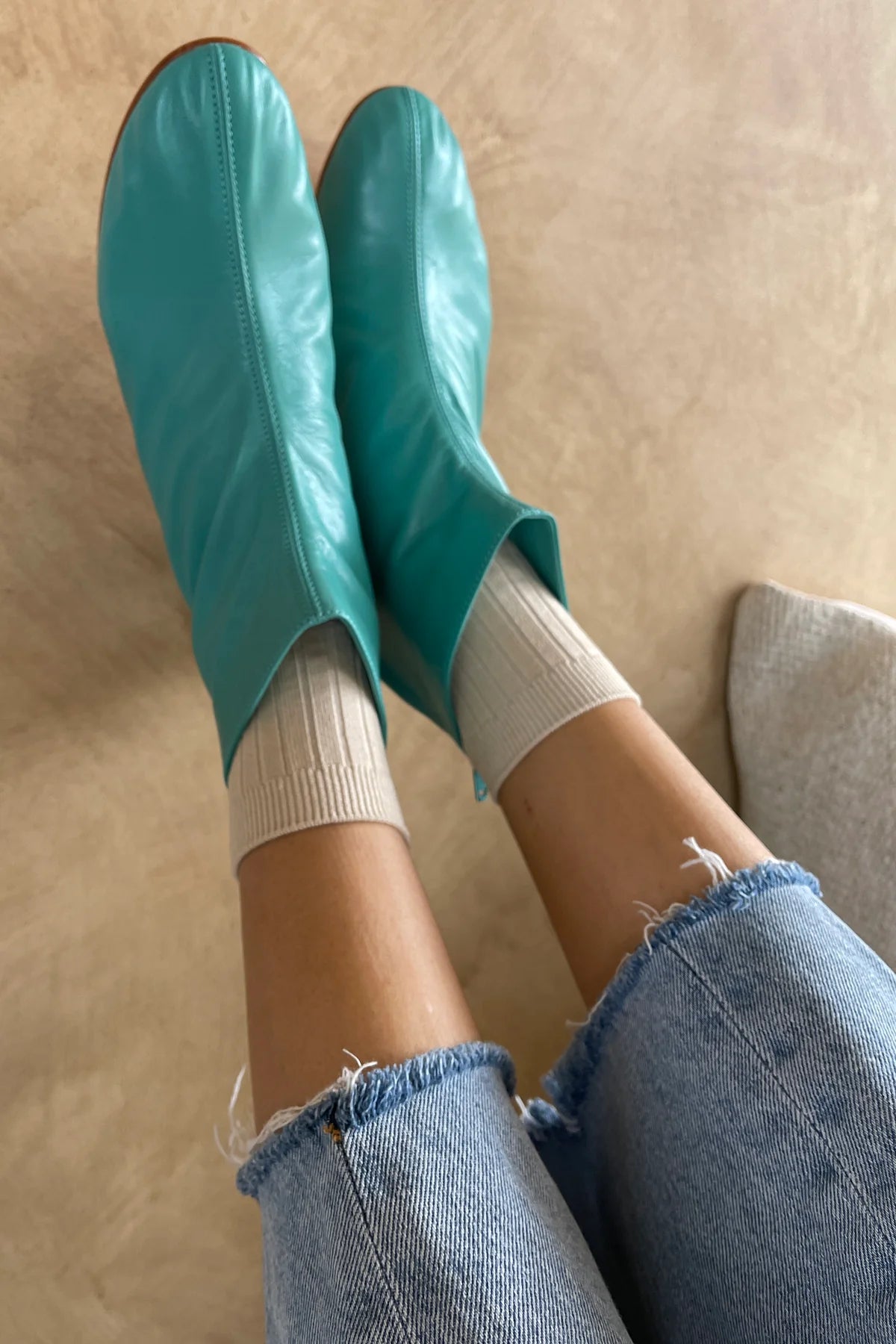 Teal rubber boots being worn on a beige surface