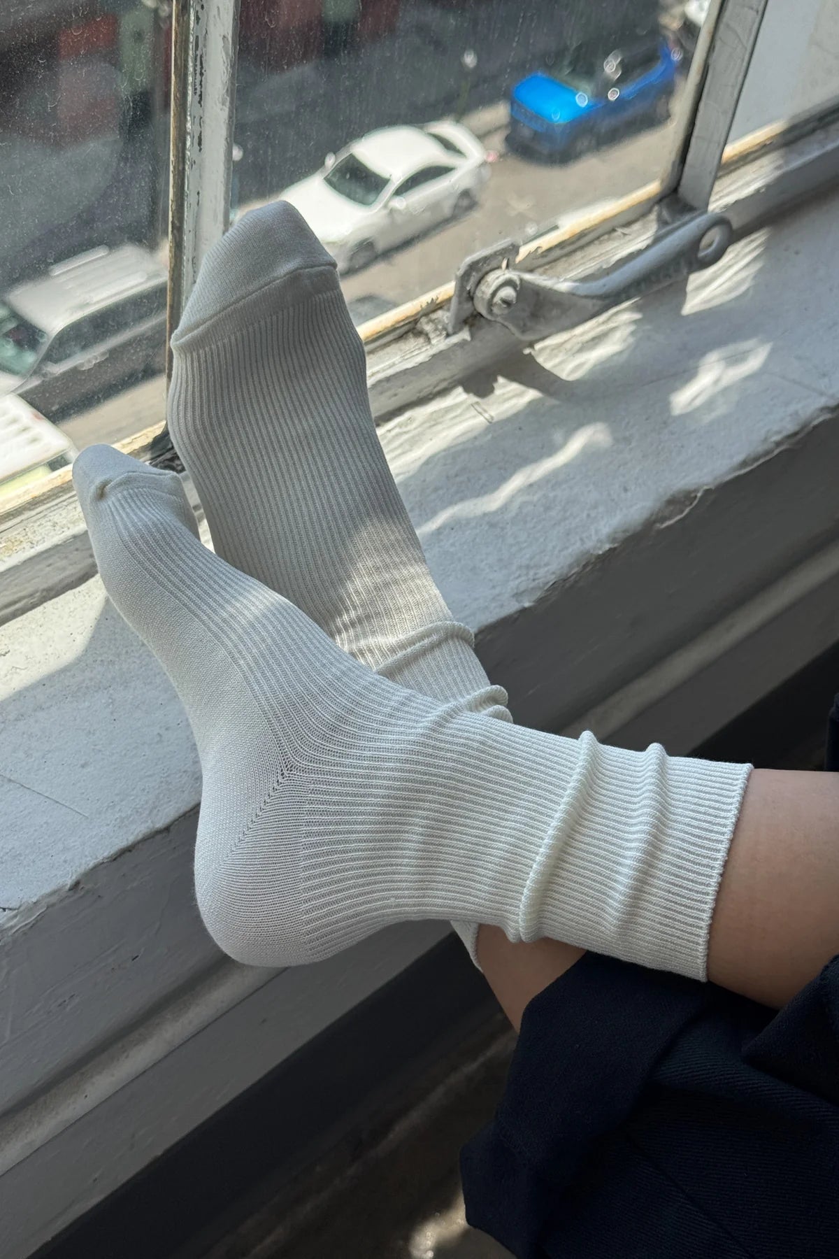 White socks hanging out of a window with a view of cars outside.