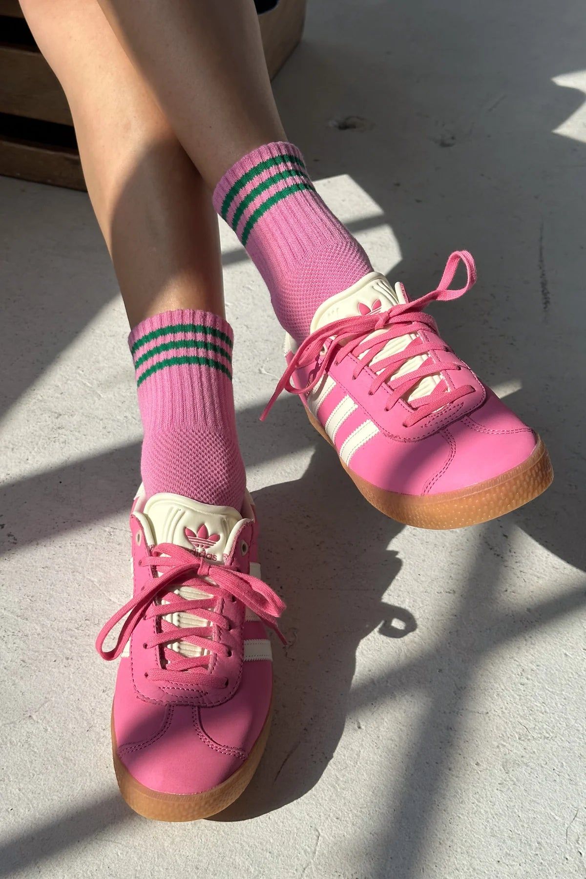 Pink sneakers with white soles and green striped socks on a concrete floor.