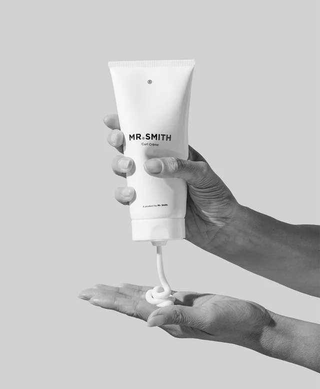 Hand holding a tube of 'MR. SMITH' cream with visible cream on the palm against a light gray background