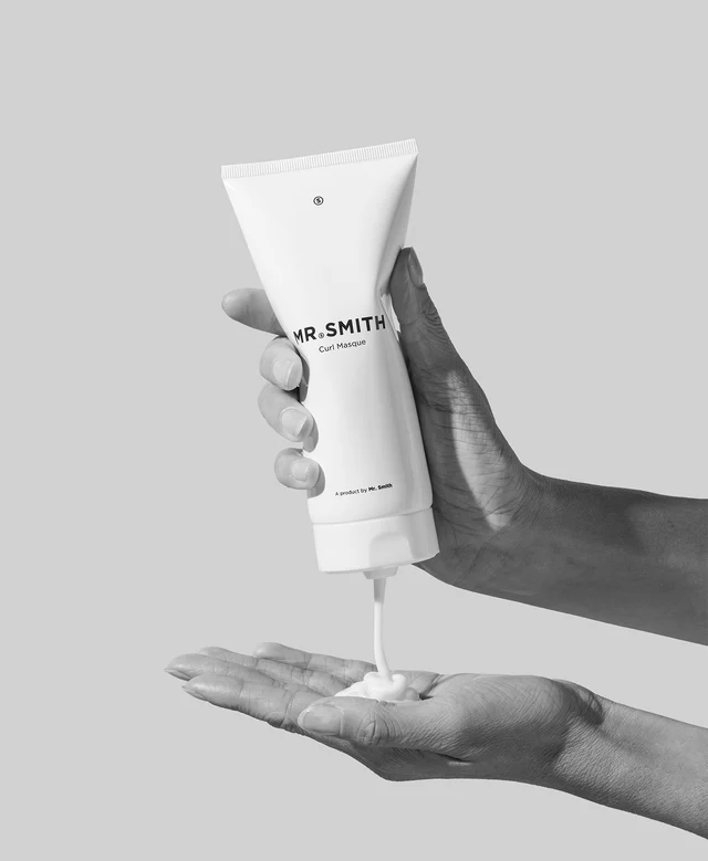 Hand holding a tube of 'MR.SMITH' cream against a gray background
