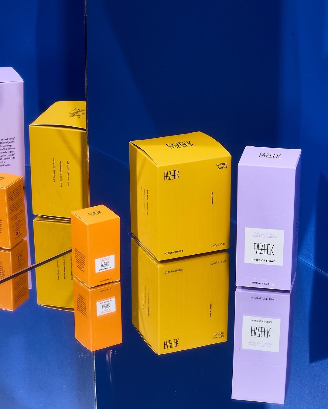 Several cosmetic boxes from the brand IARIK, including Fazeek in bright yellow and lavender, and another orange box, arranged on a reflective dark blue surface.
