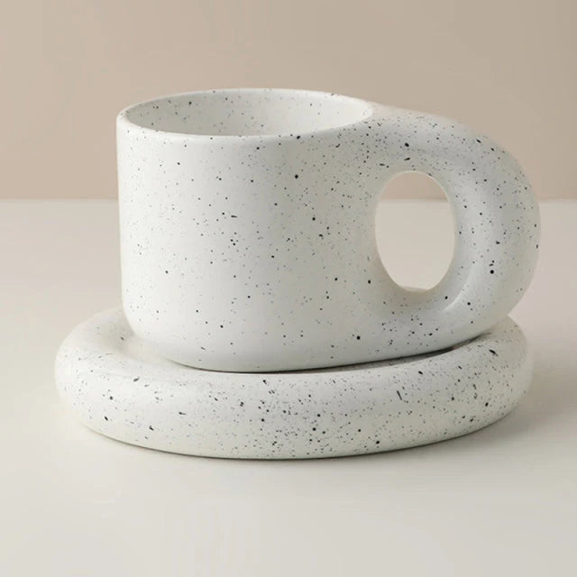 Speckled ceramic cup and saucer on a neutral background