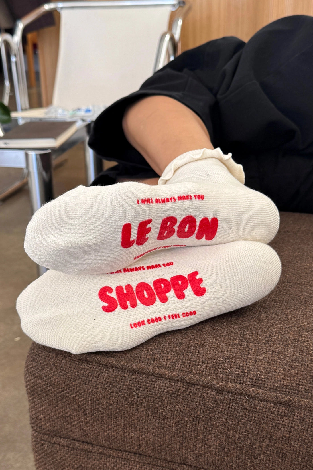 White socks with red text 'LE BON SHOPPE' worn by a person sitting on a chair.