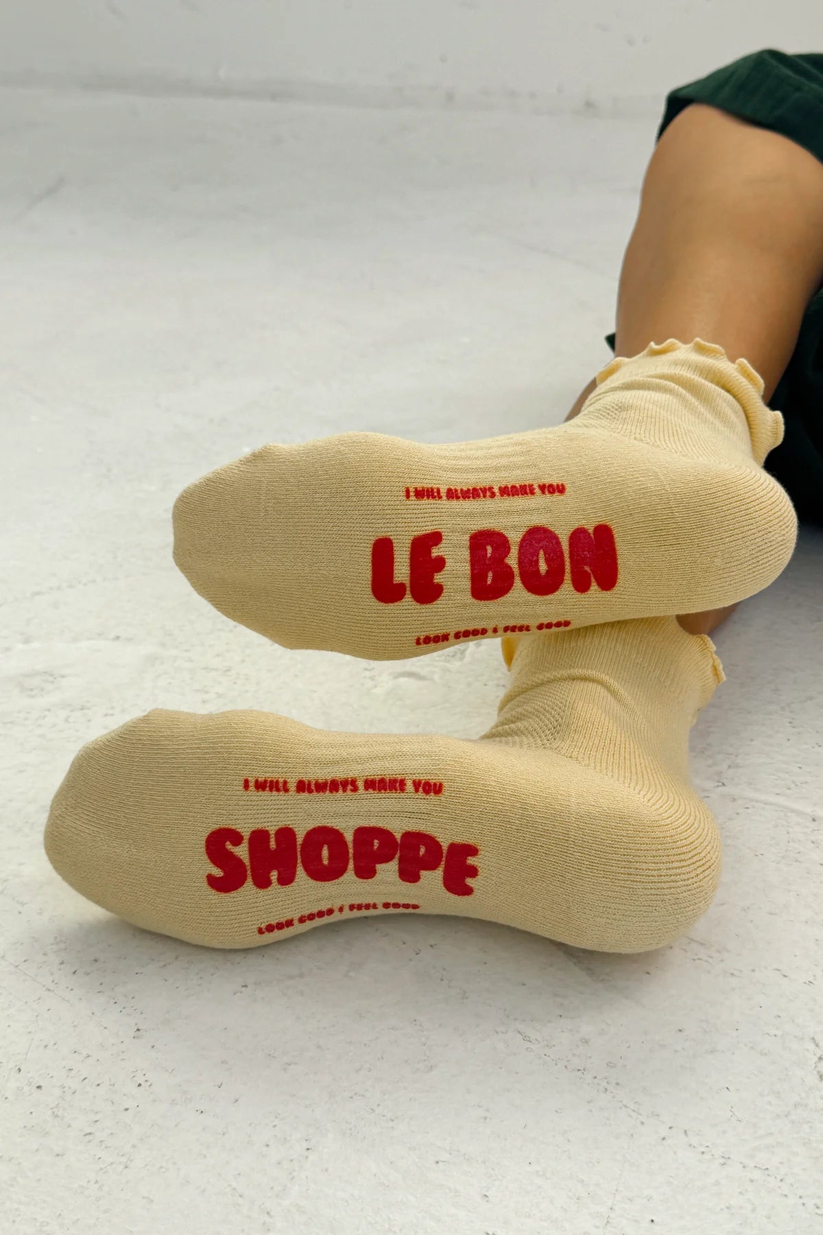 yellow le bon shoppe socks with red text worn by a person on a light gray background