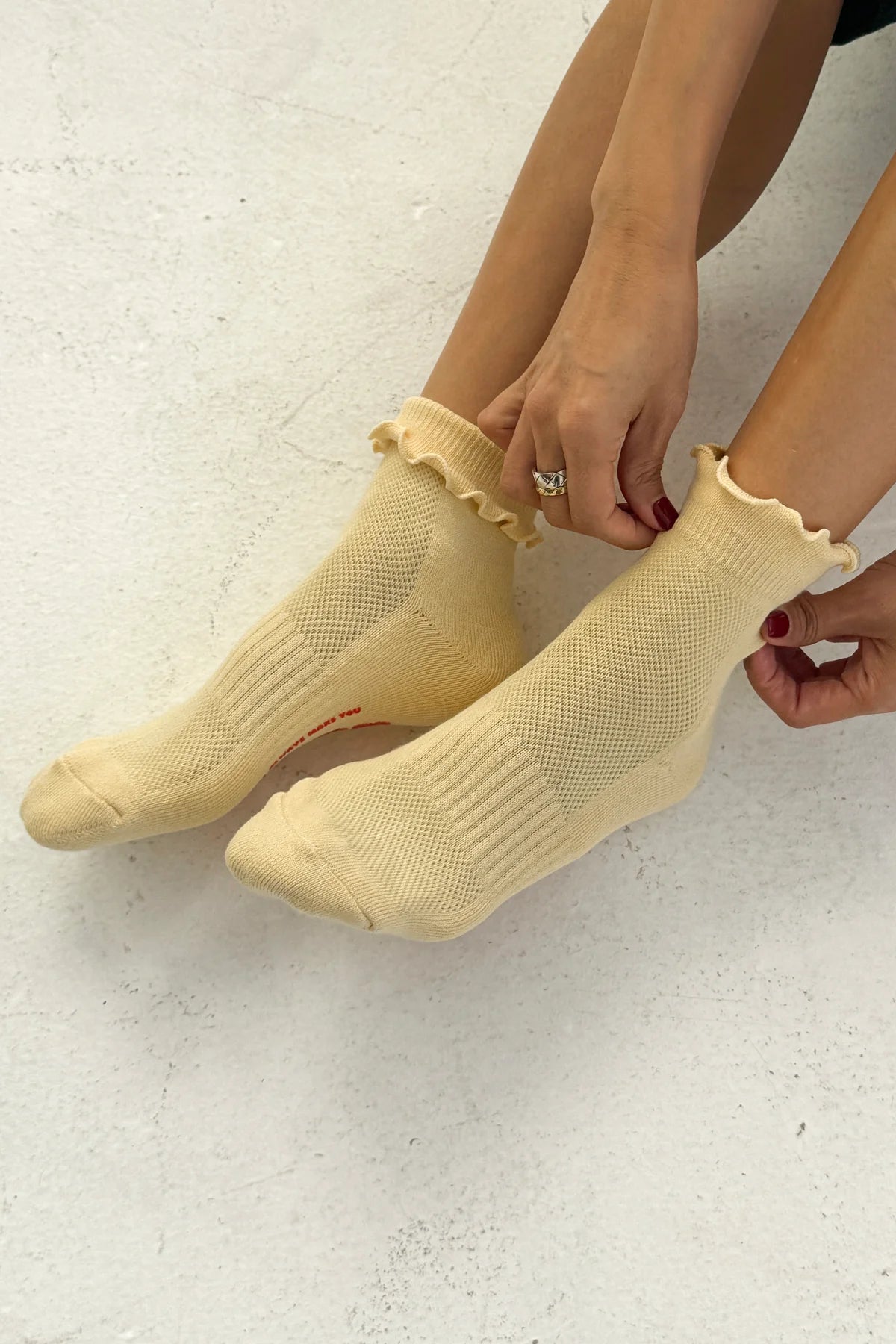 Person wearing light yellow socks with ruffled edges on a white background