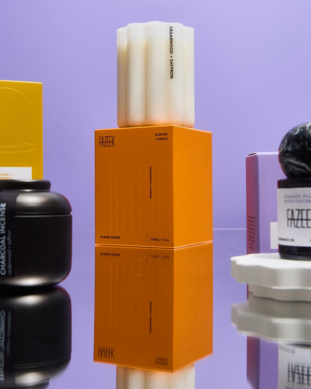 A stacked product display featuring a white rectangular bar of soap on top of an orange box, with other branded cosmetic containers partially visible around it against a lavender background.