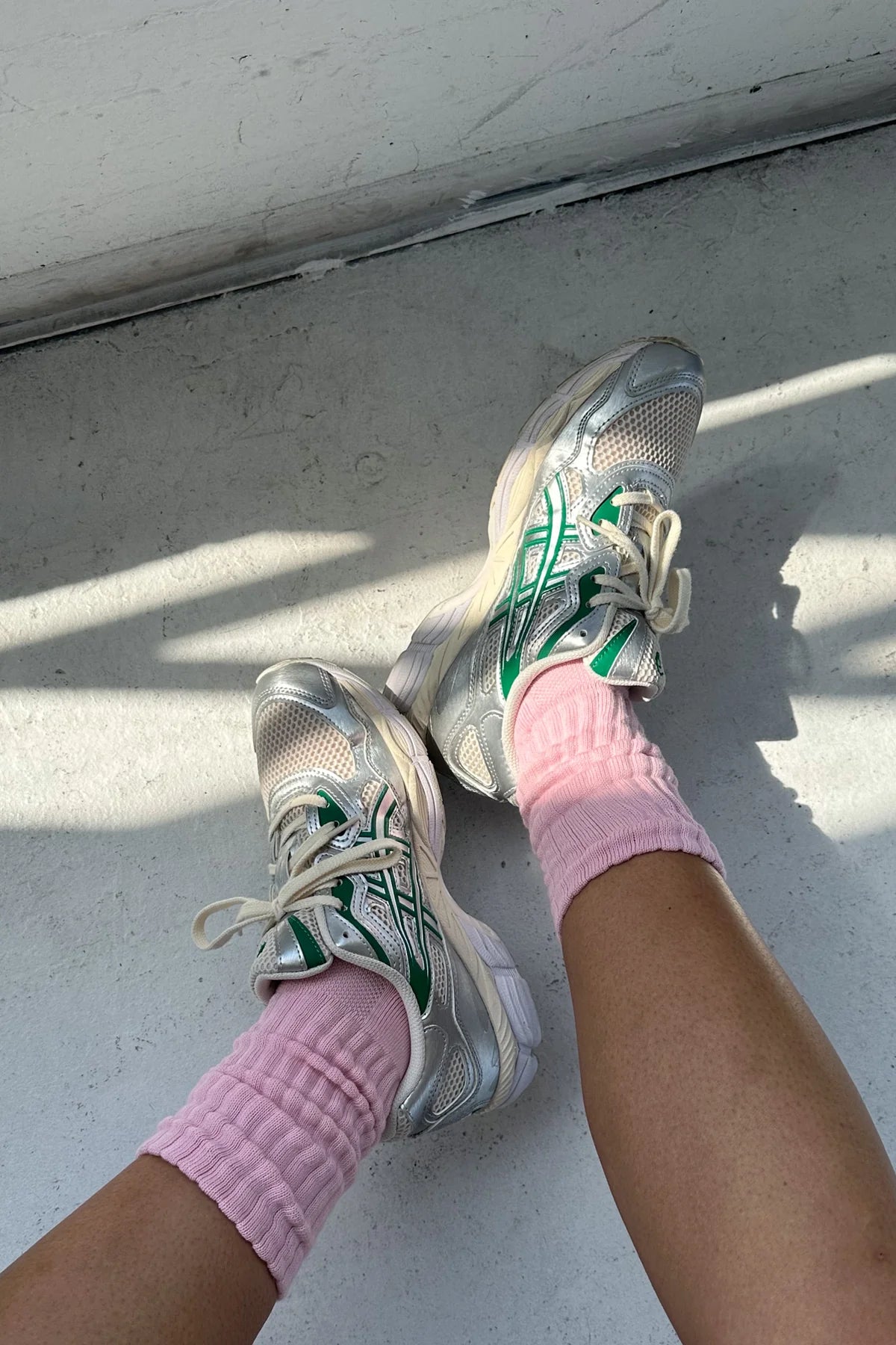 Person wearing white sneakers with green accents and pink socks on a light gray surface.