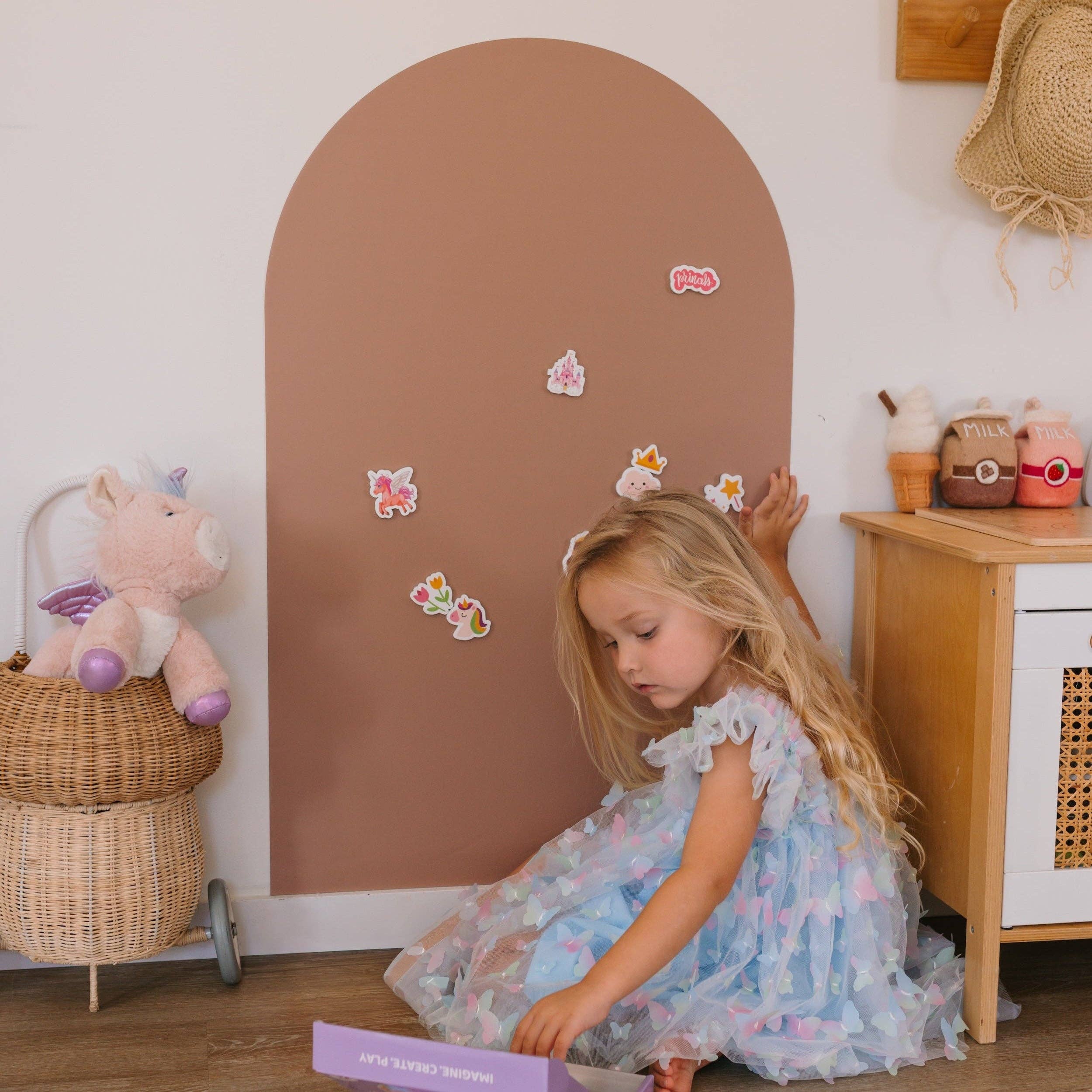 Young girl playing with a toy in a room with a brown arch and wooden furniture.