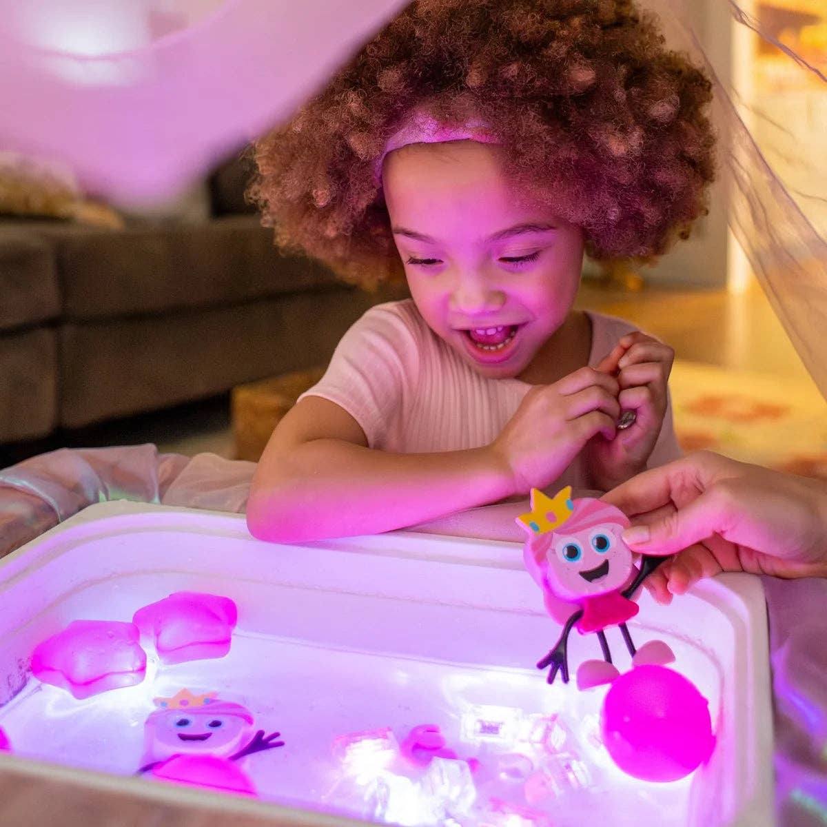 Child playing with a light-up toy under a pink canopy in a cozy living room.