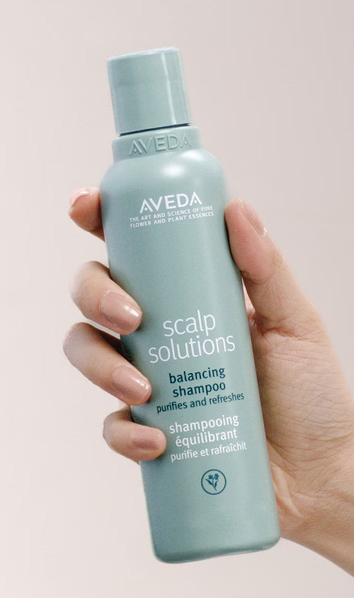 Aveda scalp solutions shampoo bottle held in a hand against a neutral background