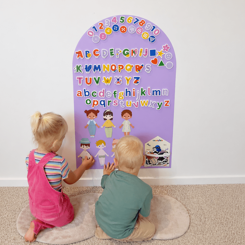 Two children interacting with a colorful alphabet chart on a white wall.