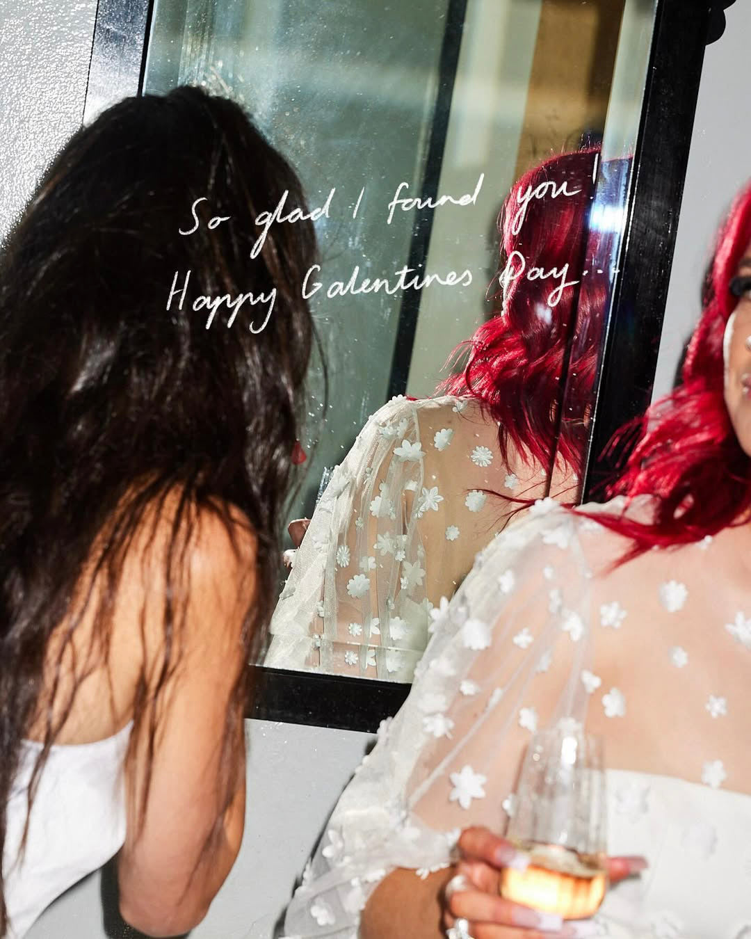 Two women in polka dot dresses looking into a mirror with a Valentine's Day message.