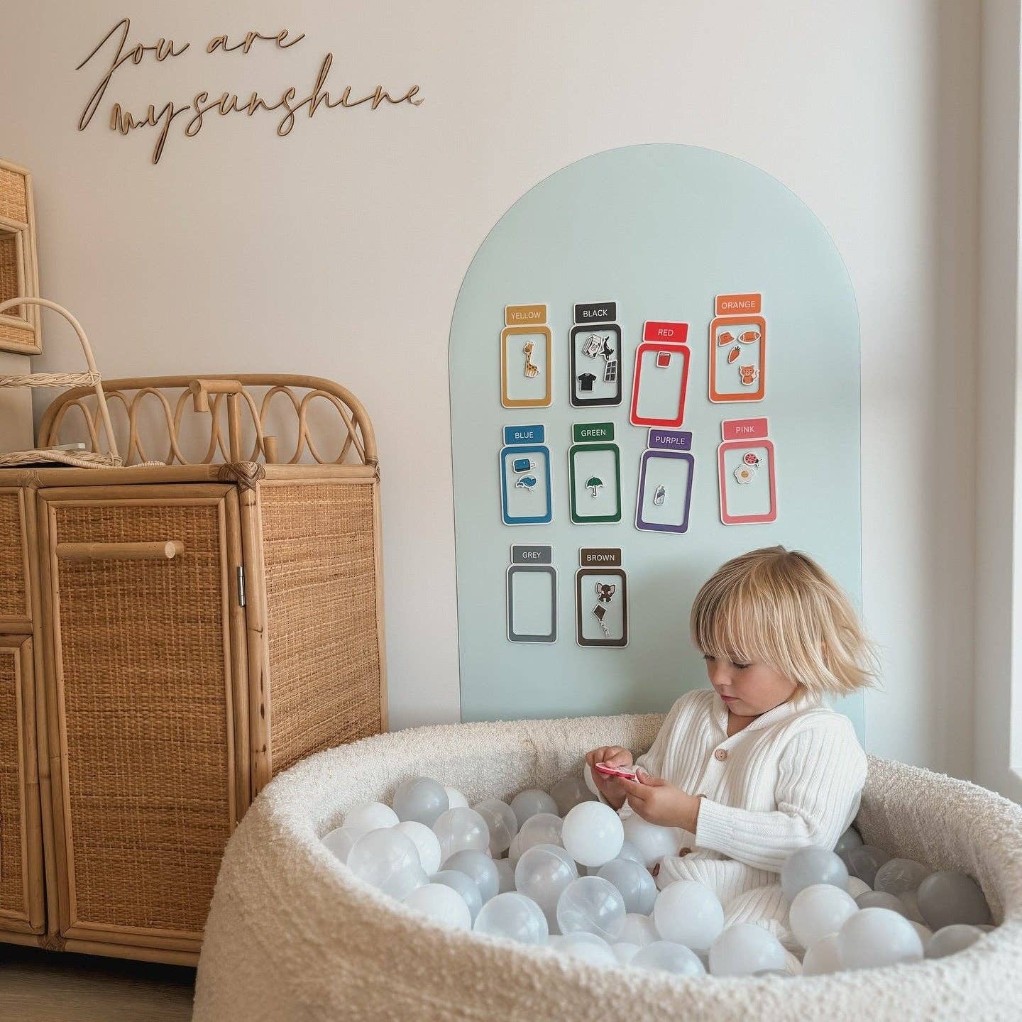 Child playing with ball pit in a cozy room with wicker cabinet and wall art.