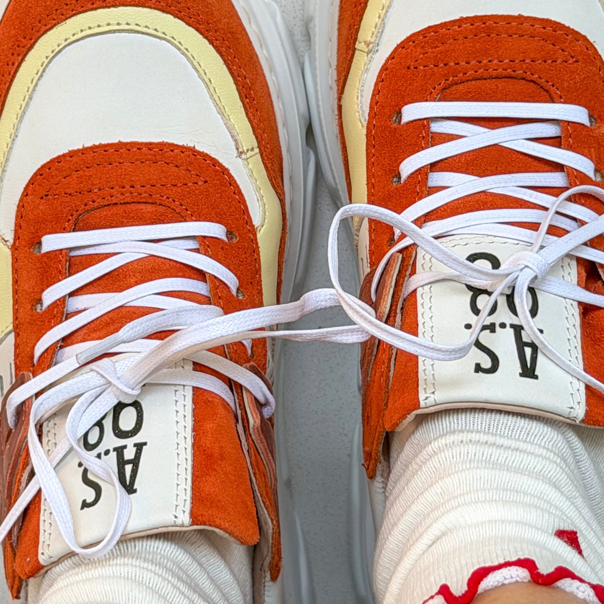 Close-up of orange and white sneakers with visible brand logo.