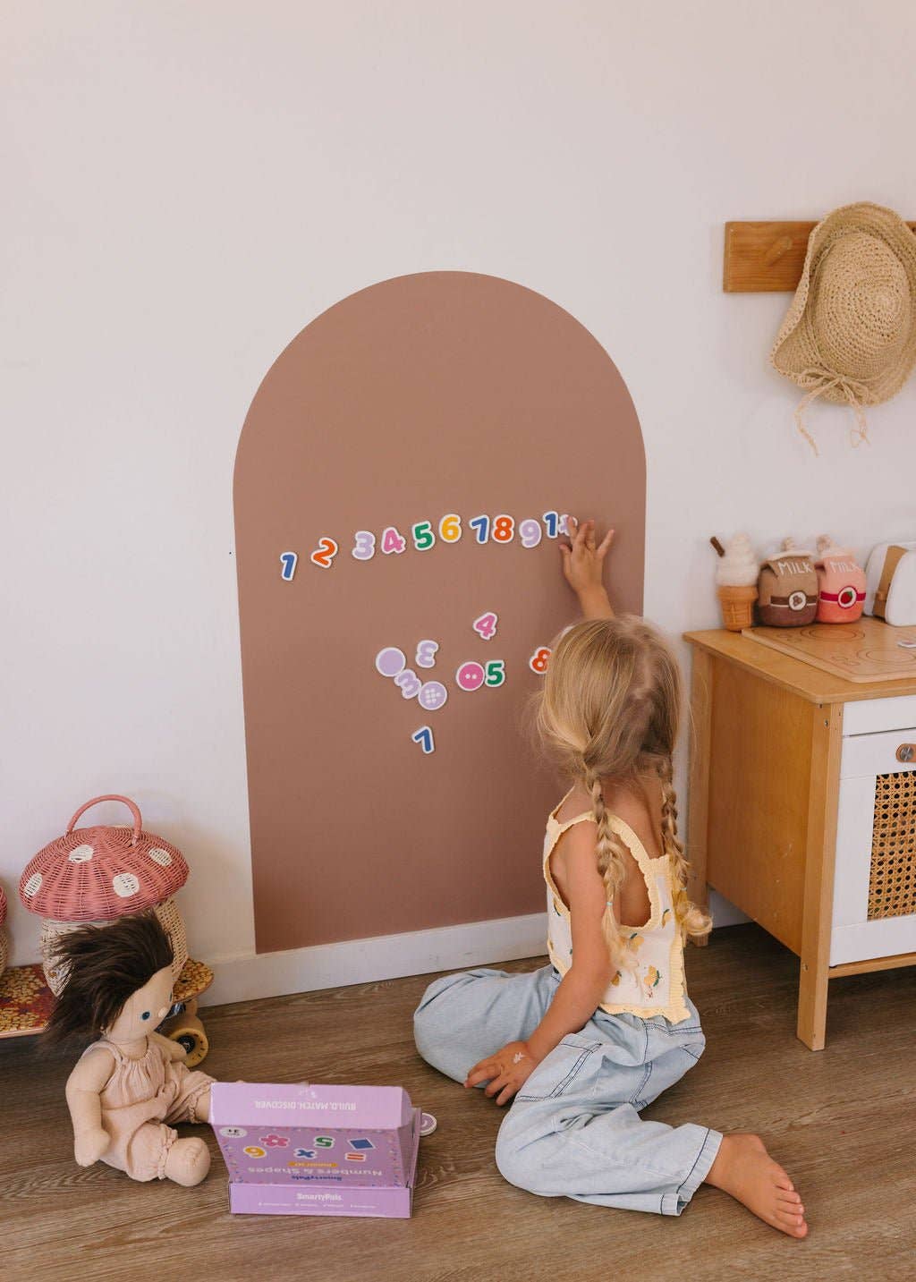 Child playing with letters on a brown arch-shaped board in a room with toys and furniture.