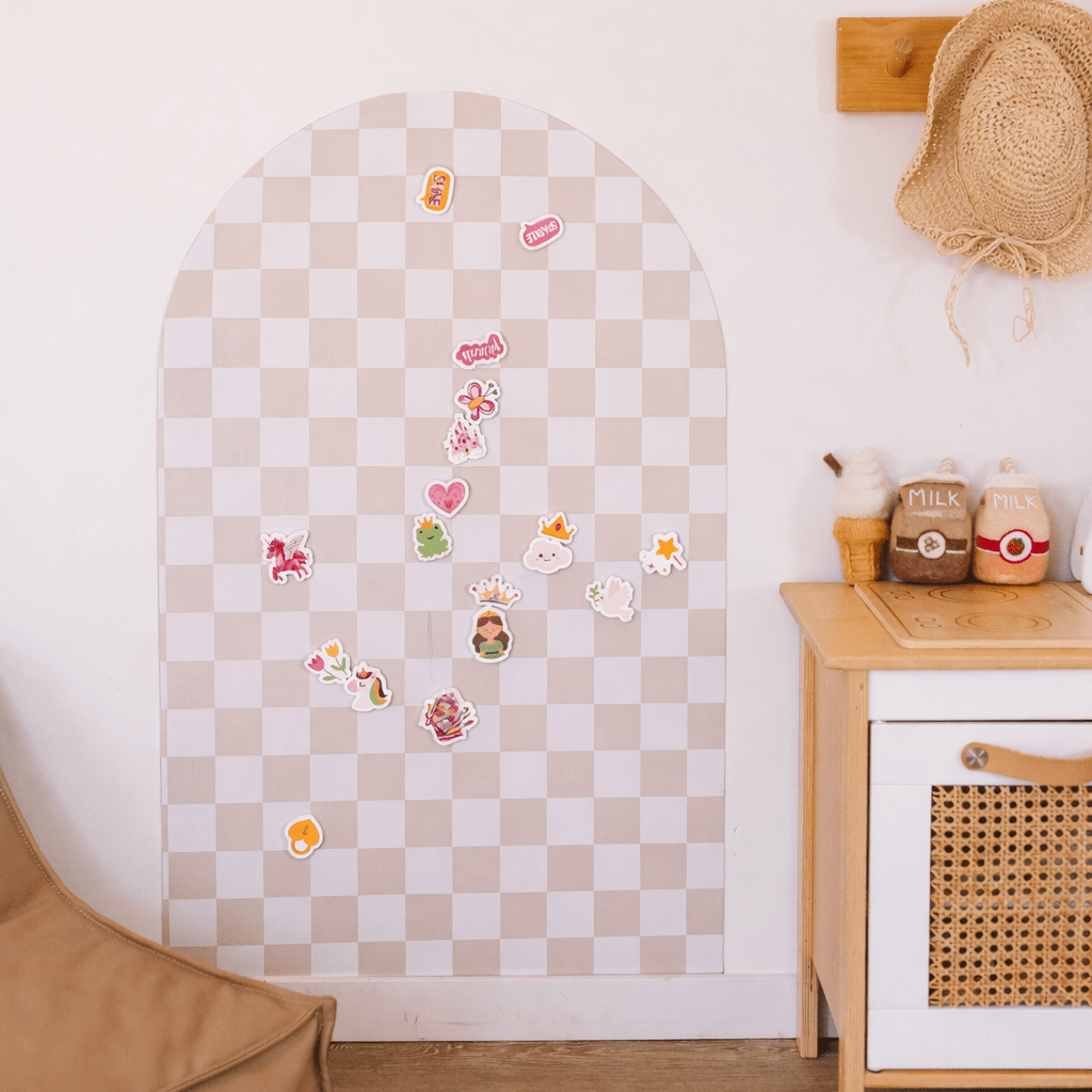 A pastel checkered arch-shaped wall organizer or board with scattered colorful stickers, shown in a styled room next to a wooden cabinet and a straw hat on a wall.