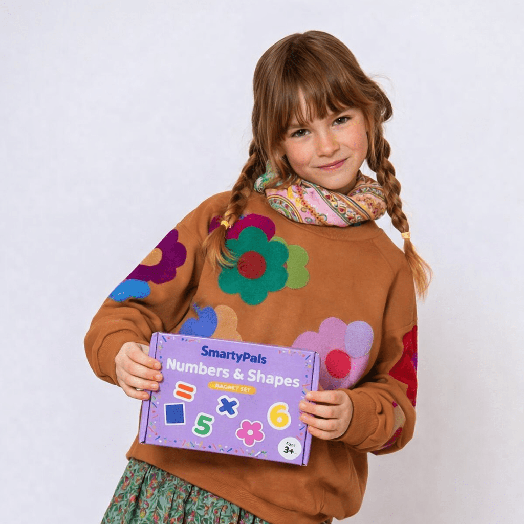 Young girl holding a SmartyPals Numbers & Shapes educational kit against a white background