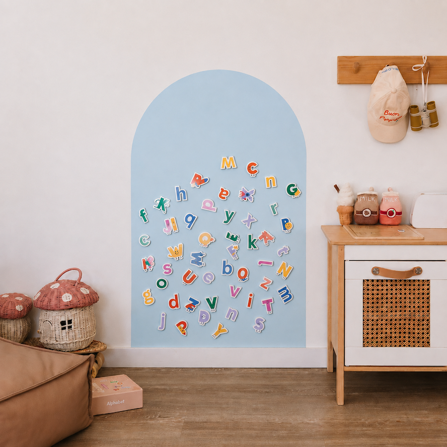 A light blue arch-shaped wall decal or magnetic board displayed on a white wall in a styled children's room. Colorful alphabet letters are scattered across the center.