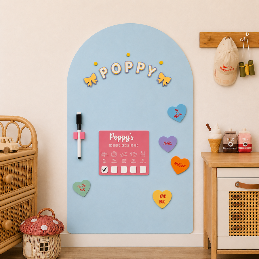 A light blue arched magnetic board with the name 'POPPY' at the top, styled in a child's room. The board includes a pink daily routine chart, small heart-shaped magnets in various colors, a black and white magnetic marker, and decorative yellow bows.