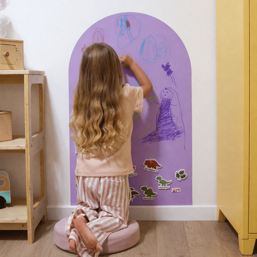 Child drawing on a purple arched wall decal in a child-friendly room.