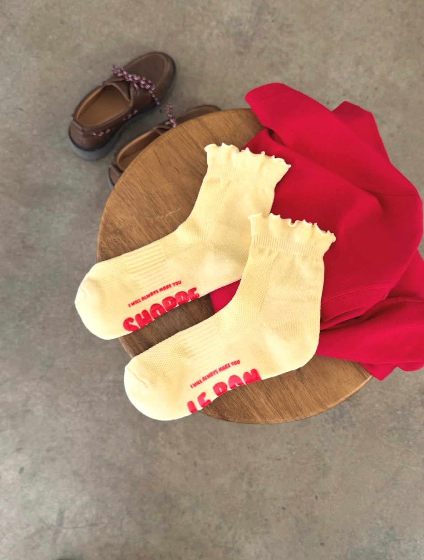 White socks with red text on a wooden block, next to brown shoes and a red garment.