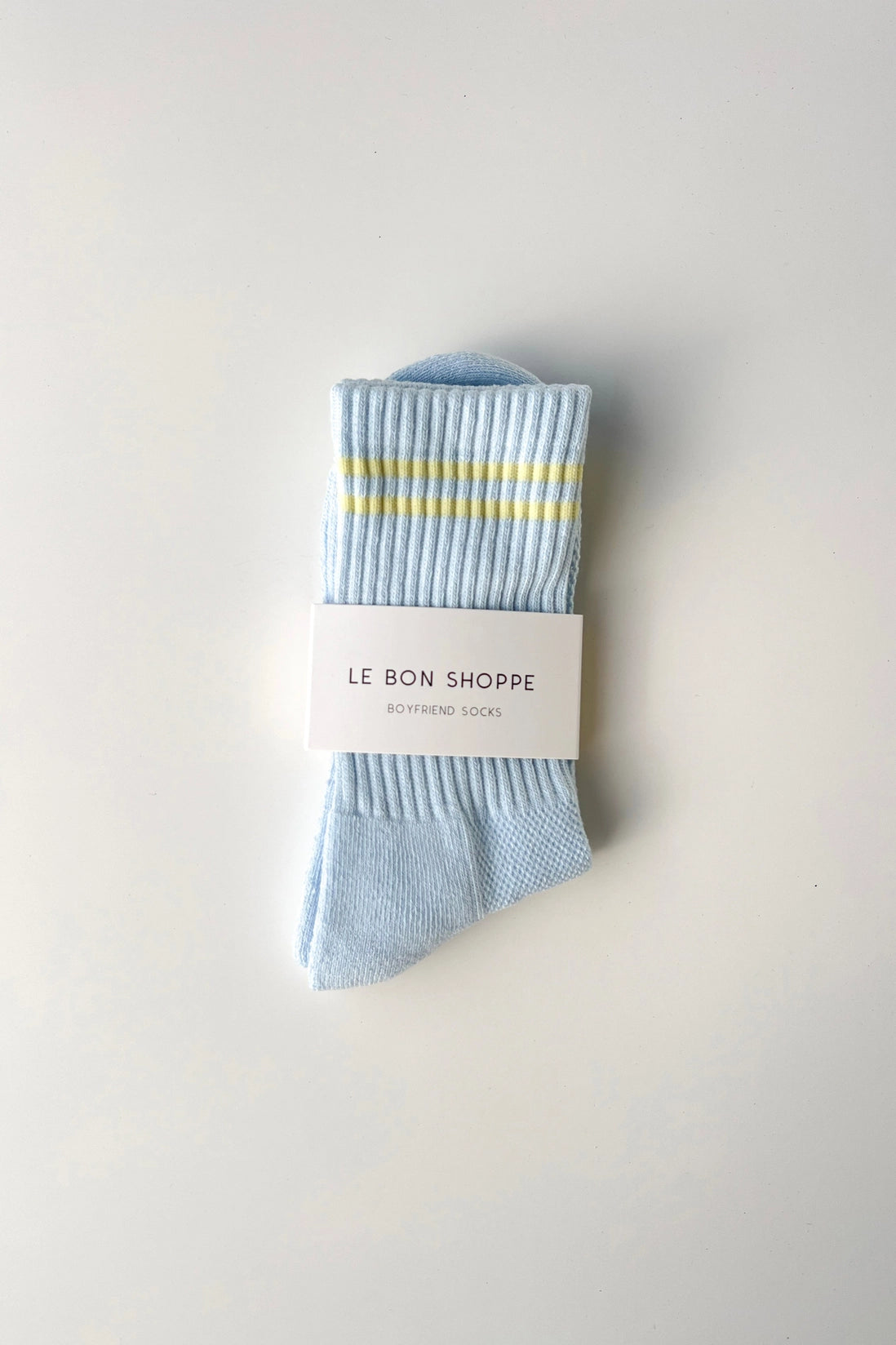 Light blue socks with yellow stripes on a white background, featuring 'Le Bon Shoppe' branding.